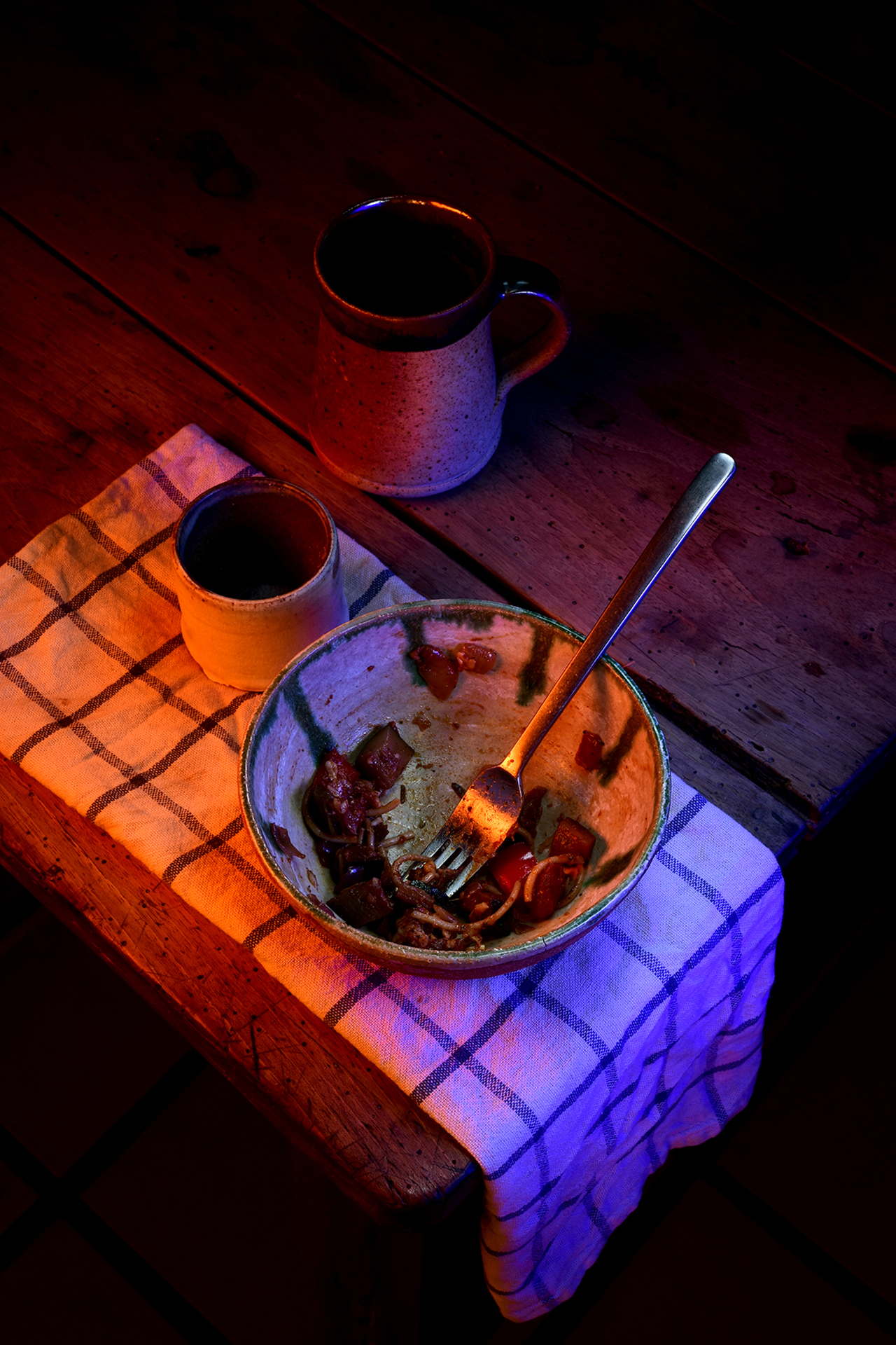 This photo depicts an empty bowl of pasta on the corner of a table, the scene is dimly lit with soft tones.