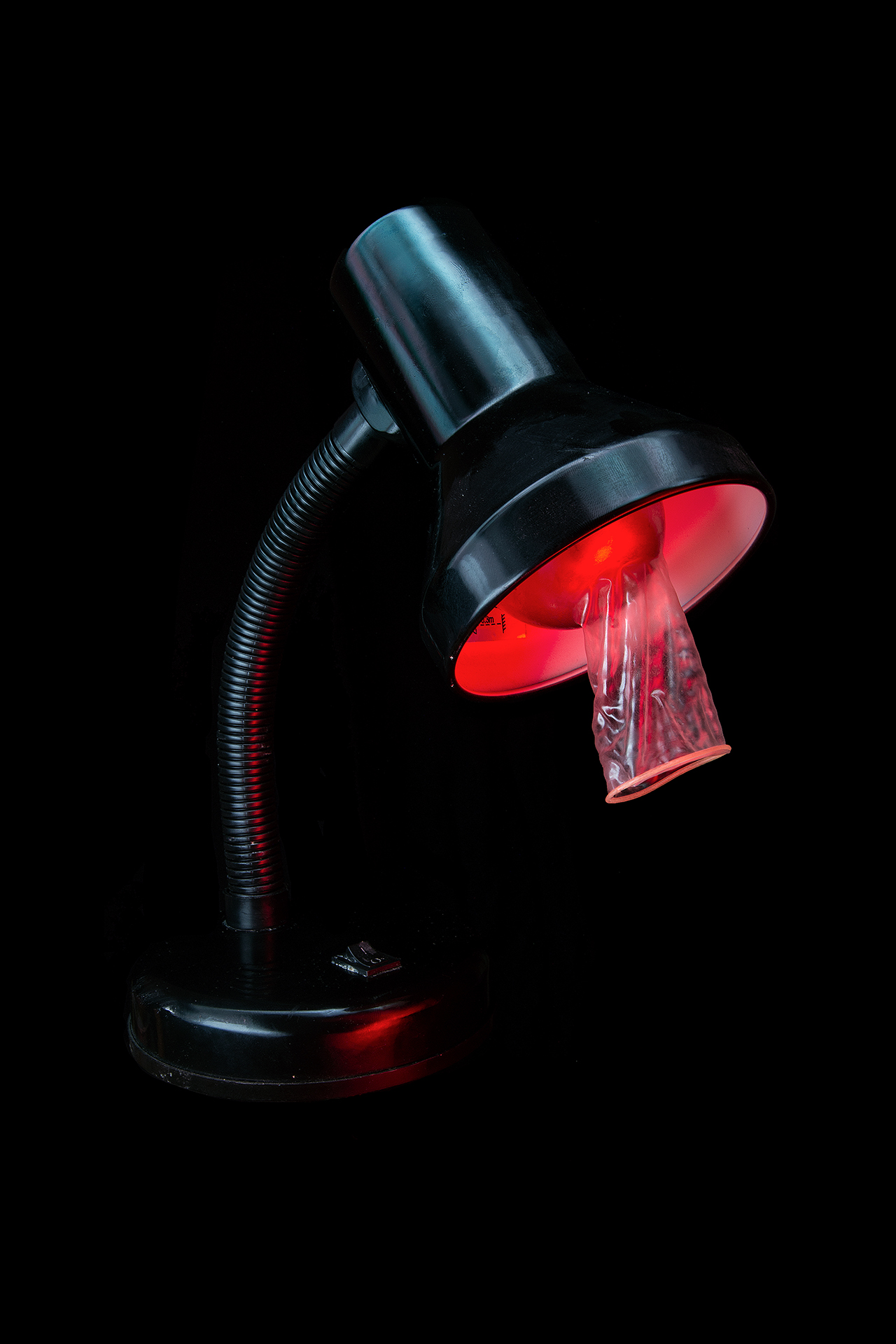 A lamp with condom on the bulb, lit with red lighting.